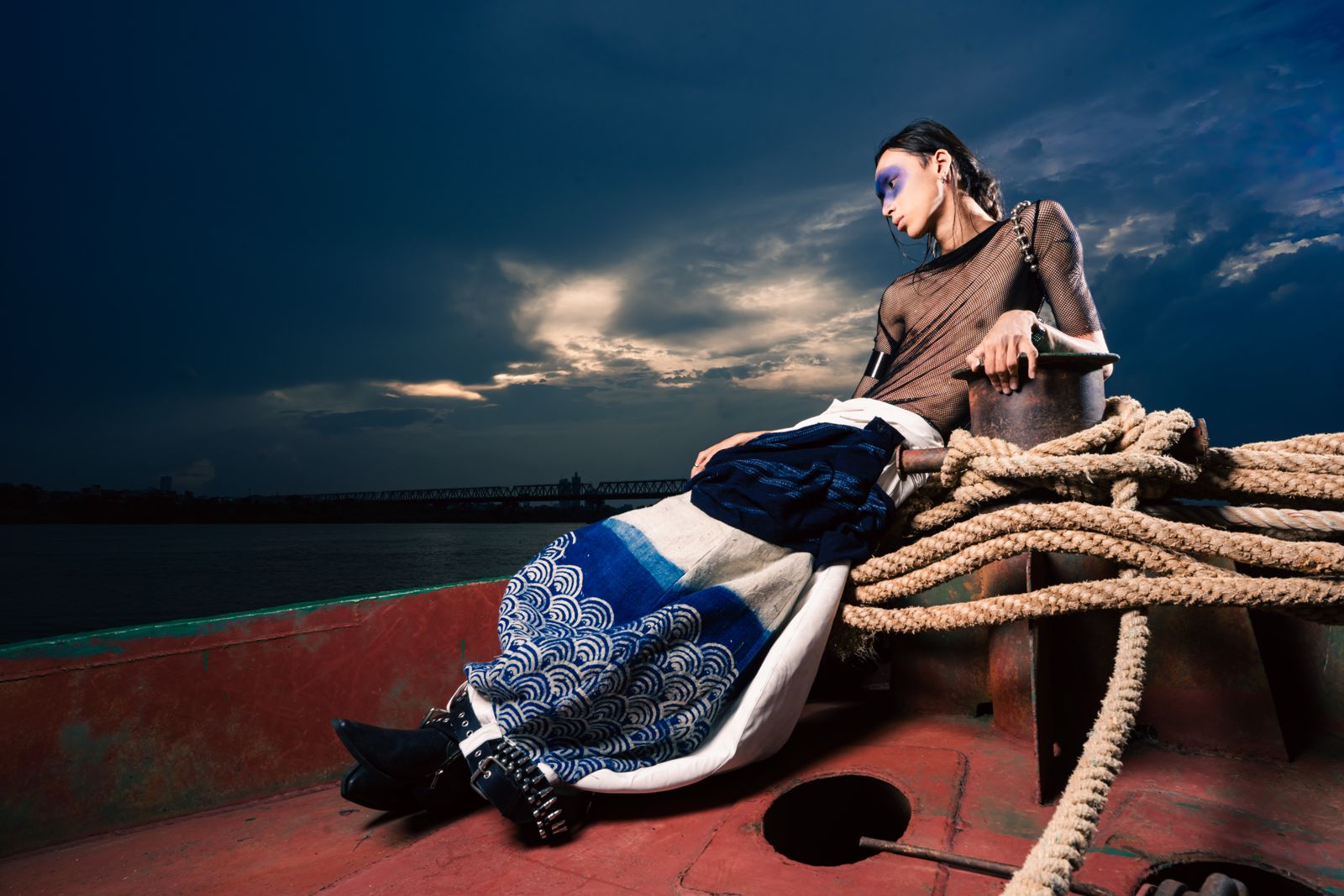 Model reclining on coiled rope on a boat deck at dusk