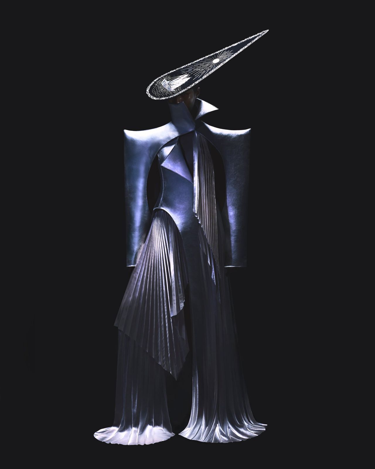 Sculptural pleated metallic gown and comet-shaped headpiece against black