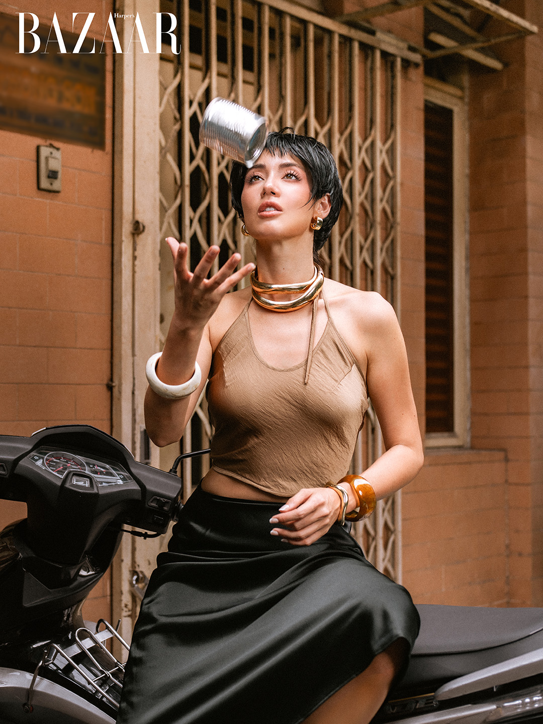 Woman on a motorbike tossing a can in front of a Saigon shopfront gate